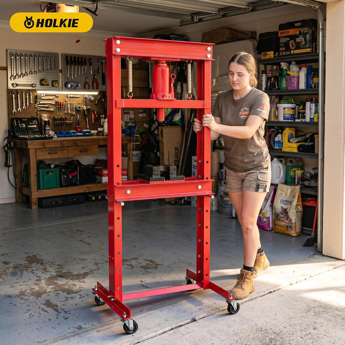 A people stands in a garage next to a red hydraulic floor press with a wheeled frame.